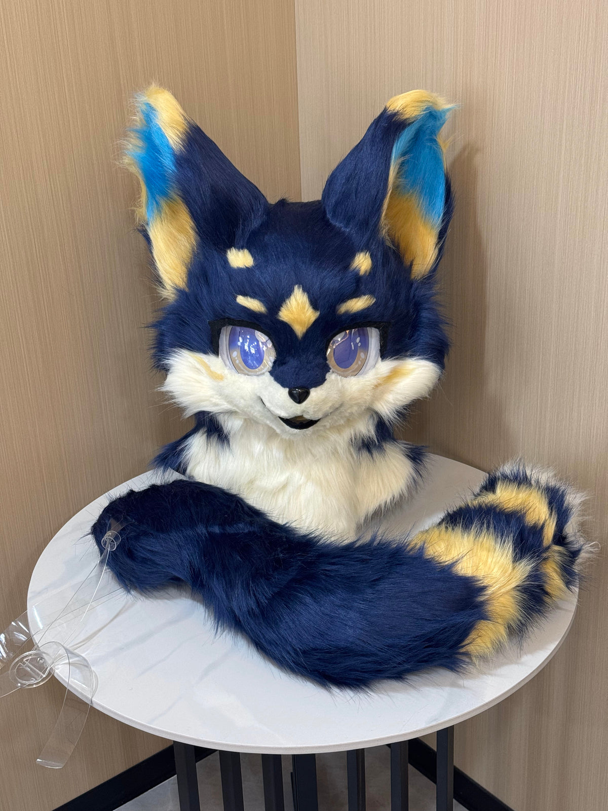 Navy blue and gold fox fursuit head with striped tail and blue eyes