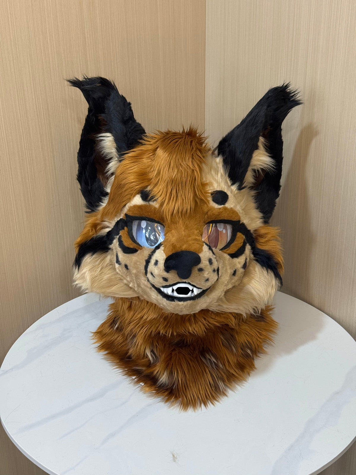 Orange and cream lynx fursuit head with tall black tufted ears and mismatched eyes